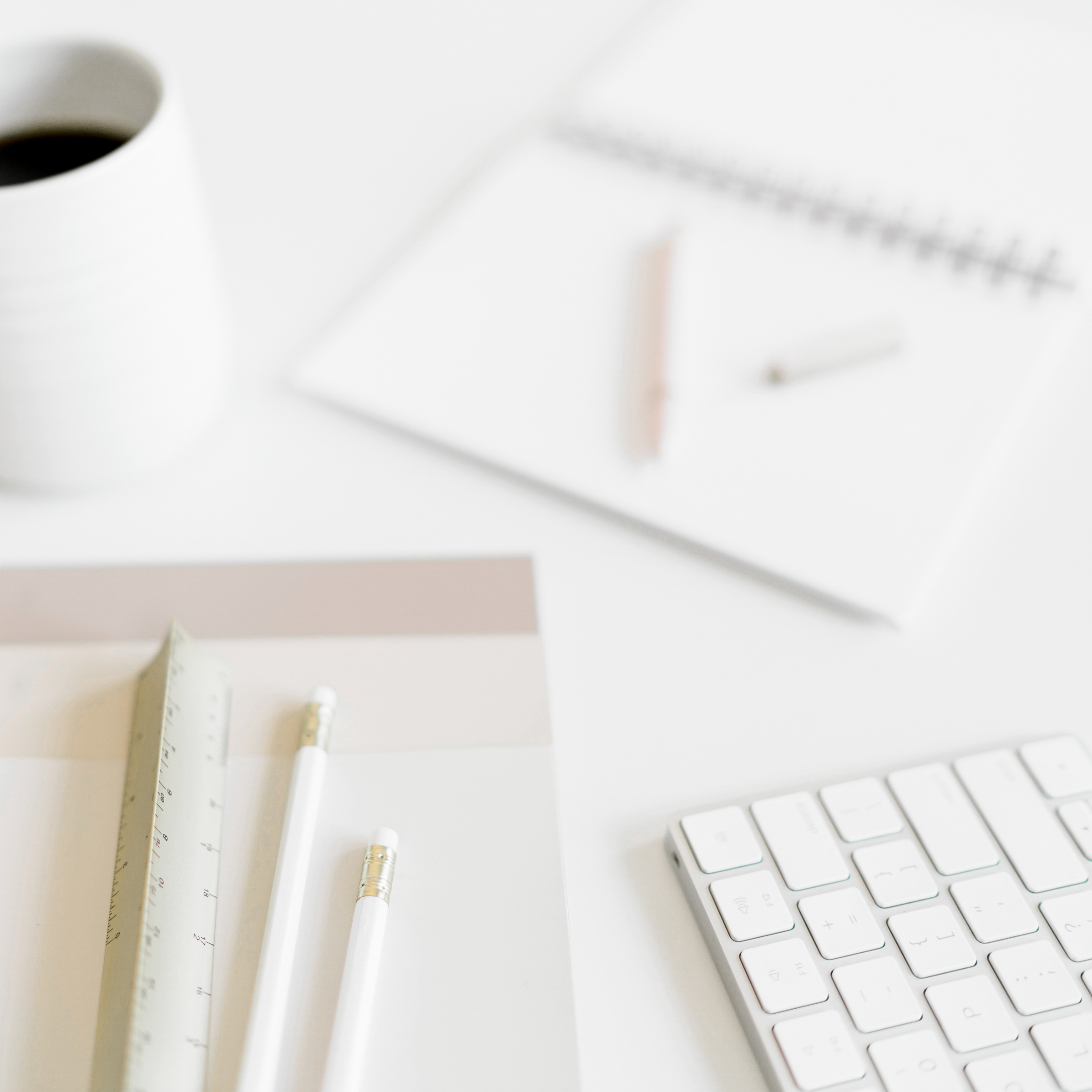 A flatlay image with a coffee, pens, keyboard and notepad